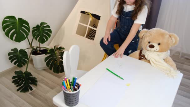 小さな女の子のサイドビューだけでふわふわのクマと白いテーブルに座って色鉛筆プレイを描画します 自宅で美しい子供のぬり絵は 創造的な活動をお楽しみくださいリラックスした 子供の遊び時間教育コンセプト — ストック動画