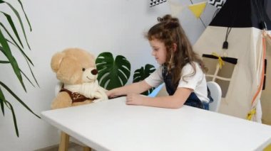 Pediatri, oyun zamanı konsepti. Pelüş ayıyla doktorculuk oynayan küçük kız çadırın yanındaki masada oturuyor. Steteskop tutan çocuk oyuncağı. Evde pofuduk hastaya hemşirelik yaparken iyi eğlenceler.