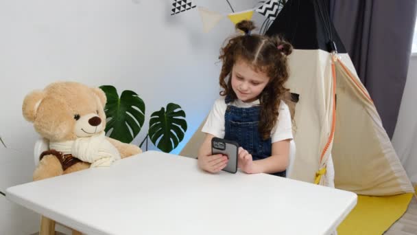 设备过度使用的概念 可爱的小女孩坐在舒适的卧室里 手里拿着智能手机 周末免费上网 看在线Vlog频道 年轻的一代沉迷于小玩艺儿 — 图库视频影像