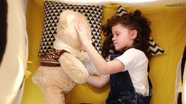 Rahat çadırda uzanan sevimli, eğlenceli küçük bir kızın en sevdiği oyuncak ayı ile oyun oynaması, güzel, küçük bir çocuğun evde okşaması. Çocukluk ve komik hafta sonu konsepti