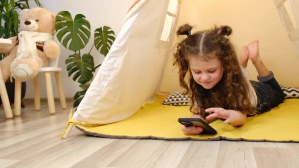 Hübsches Mädchen im Zelt liegend mit Smartphone, SMS im Messenger, Online-Spiel verbringen Zeit im Internet. Moderne Technik zum Spaß. Kinderschutz-Software für die Sicherheit von Kindern im Cyberspace