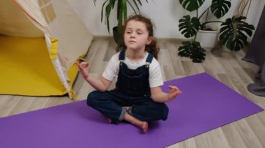 Mutlu sağlıklı kız çocuğunun yoga egzersizi yaparken, çocuk odasında sıcak zeminde otururken, evde gülüp eğlenmek için meditasyon öğretirken, gülümseyen küçük tatlı kız öğrenci.