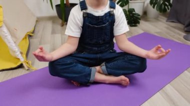 Yoga yaparak eğlenen sağlıklı kız çocuğunun yakın plan çekimi sıcak zeminde lotus pozu vererek, evde düşünceli küçük tatlı kız meditasyonu yaparak. Çocuğa duyguları yönetmeyi öğretmek, sağlıklı yaşam tarzı kavramı