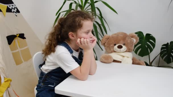 動揺ストレスの多い小さな子供は 自宅でふわふわのクマとテーブルに座って怖がっている感じ 悲しい孤独な心配している学校の子供の女の子が処罰されるか いじめられ 不幸な子供の概念を持っています — ストック動画