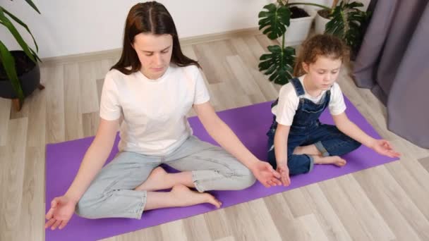 子供に感情 健康的なライフスタイルの概念を教える 静かな若い母親と小さな子供の娘座っクロス マットの上に足を閉じます目は一緒に瞑想Asanaを行います 精神的な強力な練習 — ストック動画