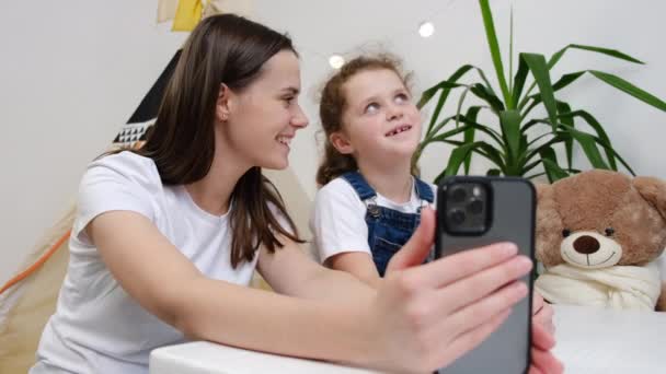 かわいい子供の娘を持つ幸せな若い母親は 携帯電話の録音Vlog 家族の影響力のあるソーシャルメディアのストリーミング 自宅でスマートフォンを使用してオンラインチャットでのビデオ通話を保持するカメラと話しています — ストック動画