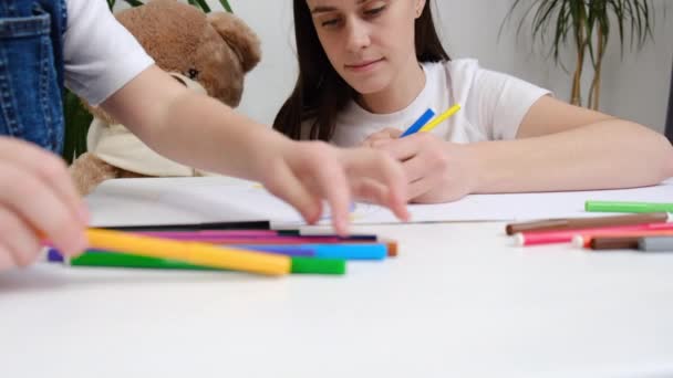 子供の発達 創造的な趣味の概念 小さな娘への着色の話を教える鉛筆で若いお母さんの絵を描くのを助ける家庭で白いテーブルに座って 優しいお母さん — ストック動画