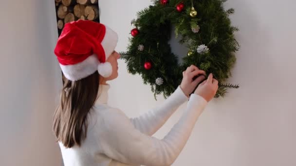 모자를 아름다운 크리스마스 화환을 장식하는 귀여운 소녀의 모습을 클로즈업 거실에서 — 비디오