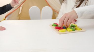 Neşeli, genç bir anne ve kız çocuğunun renkli tahta tuğlalar oynayıp oturma odasındaki beyaz masada oturmasını. Çocuk gelişimi, bebek bakıcılığı, hafta sonları ev konseptinde boş oyunlar
