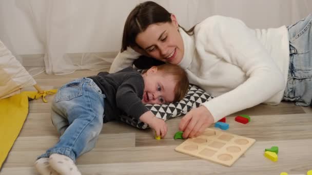 笑顔の若い母親とかわいい赤ちゃんの娘は カラフルなおもちゃのカラフルなブロックセットで遊ぶ 一緒に時間を楽しむ 床暖房システム木製の床とリビングルーム現代の家で週末を過ごす — ストック動画