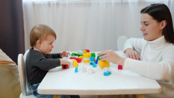 愛情のある若い母親とおもちゃを遊んでいる幸せなかわいい幼児の娘は 自宅の居心地の良い子供部屋のテーブルに座っています 週末の国内活動に関わる — ストック動画