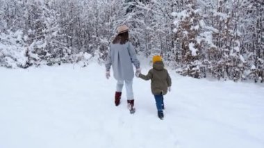 Kahverengi şapkalı, küçük tatlı kızıyla el ele tutuşan, karla kaplı ormanın yanında yürüyen, kış tatillerinin tadını çıkaran bir anne. Seyahat yaşam tarzı ve aile hafta sonu konsepti