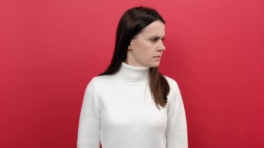 Sakin olmaya çalışan, yoga yapan, gözleri kapalı, nefes alan, beyaz örgü süveter giyen, pastel kırmızısı arka plan stüdyosuna izole edilmiş poz veren 20 'li yaşlardaki genç kadın portresi.