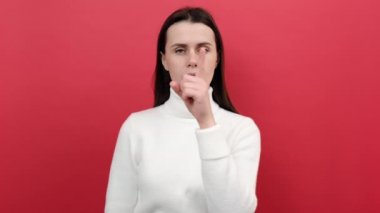 Beyaz kadın portresi, sessiz hareketler sergiliyor, sessiz kalmak istiyor, örgü süveter giyiyor, kırmızı stüdyo arka plan duvarına izole edilmiş poz veriyor. Gizli kavram tut
