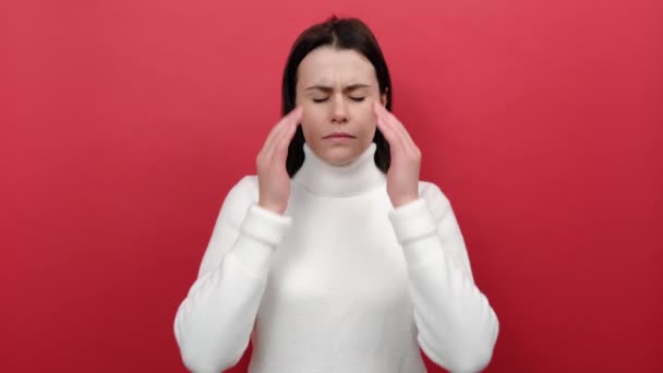 痛みを耐えられない片頭痛の苦しみから顔をしかめ 痛みの頭の上に不幸な若い女性のクラップの手を疲れ 赤い色の背景スタジオに孤立ポーズ 白いセーターを着ています 応力張力概念 — ストック動画