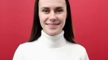 Çekici genç bayanın portresi kameraya içtenlikle gülümseyen, mutluluk ve pozitif duyguları ifade eden, rahat örülmüş süveter giyen, kırmızı arka plan stüdyosunun üzerine izole edilmiş poz veren