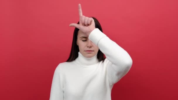 一位20多岁的不快乐的年轻黑发女子的画像 她用手指头捂住额头 对自己的失败感到沮丧 穿着白色针织毛衣 在红色背景工作室中显得孤立无援 显得很失败 — 图库视频影像