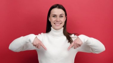 20 'li yaşlardaki mutlu genç bir kadının portresi, abone olmak istiyor ve reklam alanını tavsiye ediyor, örgü süveter giyiyor, kırmızı renkli arka plan stüdyosuna izole edilmiş poz veriyor.