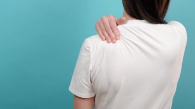 Beyaz tişörtlü, omuz ağrısı çeken, masaj yapan, reklam için fotokopi alanı olan mavi arka plan stüdyosunda izole edilmiş genç bir kadın. Sağlık ve tıbbi konsept