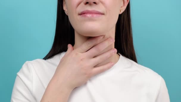 青いスタジオの壁に隔離された喉の痛みに苦しむ病気の若い女性のクローズアップ 喉の痛みの原因は インフルエンザ 一般的な風邪 細菌感染症 肺炎やアレルギーが含まれています 医学的概念 — ストック動画