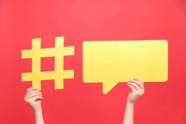 Sarı kağıt hashtag sembolü ve konuşma baloncuğu tutan kadın eller, kırmızı arkaplanda izole edilmiş ünlü medya içeriğinin esrar işareti. Viral ağ paylaşımı, blog web sitesi stratejisi kavramı