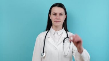 Beyaz önlüklü kadın kardiyolog, mavi arka planda izole edilmiş kamera kardiyak ilaç hapı gösteriyor. Vitamin kompleksi indirimi, etkili tedavi, kadın doktor reçeteli ilaç konsepti