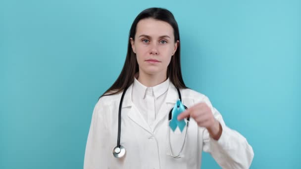 青い意識リボンと白い医療ガウンの若い白人女性医師の肖像画 世界糖尿病デーのシンボル カメラを見て コピースペースでスタジオの背景に隔離されたポーズ — ストック動画