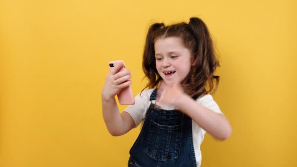 快乐的小女孩拿着电话录音机和摄像机聊天 影响社交媒体流 用智能手机在网上聊天 在黄色的工作室背景下摆出孤立的架势 — 图库视频影像