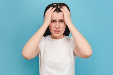 Stresli, sağlıksız bin yıllık kadın migren, panik atak ve yüksek tansiyon yüzünden yorgun hissediyor. Bitkin düşmüş genç bir kadın baş tapınaklarına masaj yapıyor, mavi stüdyo arka planında poz veriyor.