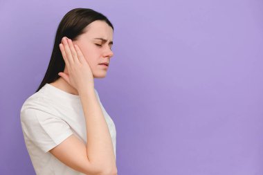 Üzgün, genç, beyaz bir kadının acı veren bir kulağı olduğunu, aniden güçlü bir ağrı hissettiğini, menekşe rengi arka plan duvarında izole edilmiş bir poz verdiğini ve tavsiye için fotokopi çekildiğini düşünün. Sağlık sorunu kavramı