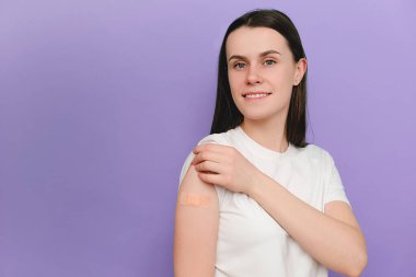 Kadın covid-19 'a bağışıklık kazanıyor önerilen aşı, koronavirüs programı, mor arka planda boş alan. Kadın hasta aşıdan sonra omzuna yara bandı yapıştırıyor.