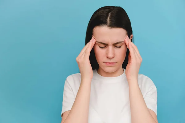 近距离观察疲惫而悲伤的年轻高加索女人头痛 蓝底模型与复印空间 头痛的原因包括偏头痛 紧张性头痛 抑郁或脑瘤 — 图库照片