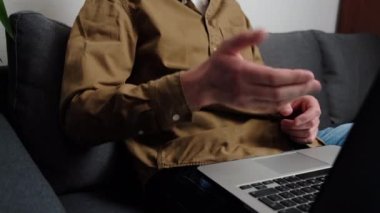 Gri koltukta oturan genç adamın seçici odak noktası kucağında bilgisayarla, arkadaşlarıyla ya da ailesiyle sanal etkinliğin keyfini çıkarırken, web kamerasıyla konuşma ya da iş arkadaşlarıyla görüşmeler yaparken.