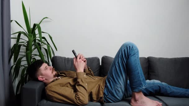 Молодий Чоловік Який Лежить Дивані Тримає Смартфон Вільний Час Інтернеті — стокове відео