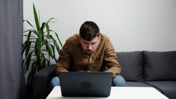 沉思严肃的男人坐在灰色沙发上 带着笔记本电脑在家里 做决定 专心致志的留胡子男人想着困难的网上项目 信息分析与问题解决的概念 — 图库视频影像
