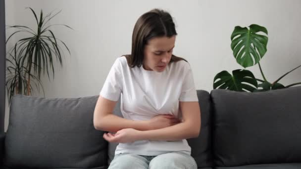 Αγχωμένη Νεαρή Γυναίκα Κάθεται Στον Καναπέ Αγκαλιάζει Την Κοιλιά Υποφέρει — Αρχείο Βίντεο