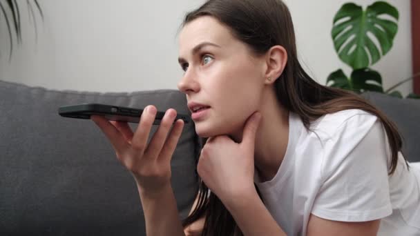 一个可爱的年轻女人靠在沙发上 用智能手机捂住嘴 用扩音器和男朋友说话 语音短信 智能虚拟助手 现代电子技术概念的应用 — 图库视频影像