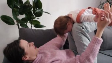 Değer veren genç bir anne sırt üstü rahat bir kanepede uzanıp küçük kızını dizlerinin üzerine çökmüş halde kucağında tutuyor. Tasasız çocuk kız uçuyor gibi davranıp annesiyle jimnastik yapıyor. Oyun uçma konseptini taklit et