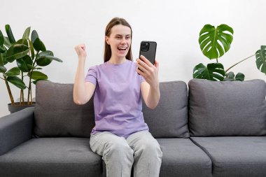 Heyecanlı mutlu kadın kazanan cep telefonuna bakarak başarı kavramını kutlayan bir uygulama kullanıyor. Neşeli genç bayan müşteri kazanan teklifi kutluyor ya da akıllı telefondan ecommerce alışveriş teklifi alıyor.