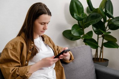 Sakin bir genç kadın evde boş zamanını oturma odasındaki rahat kanepeye oturup akıllı telefondan mobil uygulamayla mesaj atarak geçirir. İnternetteki esmer kız sohbetini kapat ve çevrimiçi izlemek için cep telefonunu kullan.