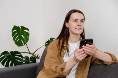 Güzel, mutlu genç bir kadın, hafta sonunu evde, kanepede oturarak, elinde akıllı telefonuyla, erkek arkadaşıyla uzaktan sohbet ederek, pencereden dışarıyı seyrederek, güneşli, tasasız bir günün tadını çıkararak geçirir.