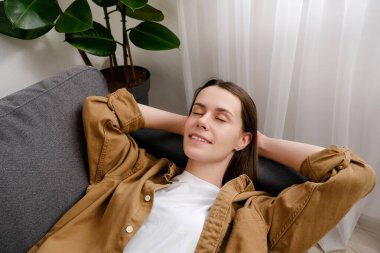 Genç, dingin, esmer bir kadının kanepeye uzanmış, derin bir nefes alıp, el ele tutuşup, rahat bir şekilde kanepede kestirip dinlenen sağlıklı, sakin bir kız. Evde stres yok.