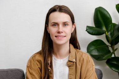 Genç, çekici, mutlu, beyaz kız öğrencinin yakın portresi ya da modern evde kameraya bakarak poz veren profesyonel bir öğrenci. Güzel, tatlı esmer kadın. 20 'li yaşlarda. Hafta sonunun tadını çıkar.