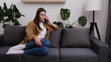 Endişeli genç bir kadın telefonla arıyor, akıllı telefonla konuşuyor, evde yalnız başına kötü haberler alıyor. Ayrılık, stres, işte ya da ilişkilerde sorunlar, korku, olay olduğunda endişe. Negatif insan duyguları