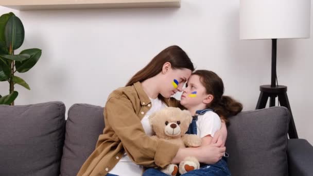 乌克兰有爱心的年轻母亲和不快乐的小女儿坐在沙发上抱着毛茸茸的熊 悲伤地看着相机 停止来自俄罗斯的侵略 儿童反对 — 图库视频影像