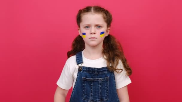 脸上挂着乌克兰国旗的严肃小女孩的画像表现出停止动作 孤立在红色的背景墙上 俄罗斯对乌克兰的入侵 儿童反战 军事冲突 — 图库视频影像