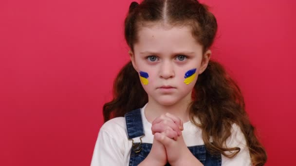 失望的小女孩 脸上挂着乌克兰国旗 因红色背景 信仰和希望的姿态而被隔离 儿童反对战争 俄罗斯入侵乌克兰 请求国际社会的帮助 — 图库视频影像