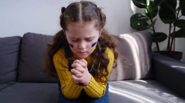 Umut dolu küçük kız evdeki kanepede oturan, yüzünde Ukrayna bayrağı olan bir çocuk için dua etmeye devam ediyor. Çocuklar savaşa karşı. Rusya 'nın Ukrayna' yı işgali, dünya toplumunun yardımını istiyor