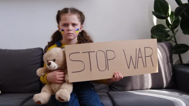 乌克兰小女孩拿着写着 停止战争 字样的横幅抗议战争冲突 毛茸茸的熊宝宝坐在沙发上 停止侵略 儿童反对俄国战争 — 图库视频影像