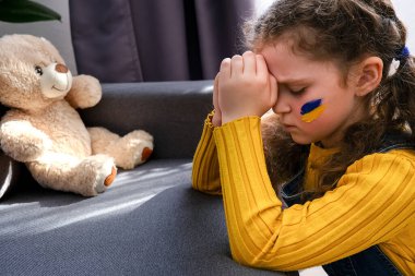 Umut dolu küçük kız çocuğu dua etmeye devam ediyor. Ukrayna bayraklı çocuk evde oturuyor. Çocuklar savaşa karşı. Rusya 'nın Ukrayna' yı işgali, dünya toplumunun yardımını istiyor